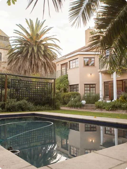 Swimming pool in front of a two-storey house framed by palm trees