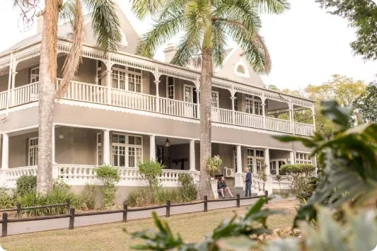 Two-storey building with long wraparound verandas, surrounded by palm trees