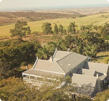 Aerial view of a large farmhouse among trees, with rolling green hills beyond